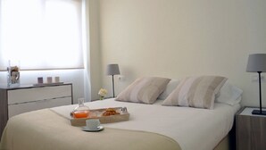 A neatly made bed with pillows, a bedside table with a lamp, a tray with breakfast items, and a window with curtains.