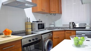 A modern kitchen with wooden cabinets, stainless steel appliances, a microwave, a coffee maker, and a washing machine.