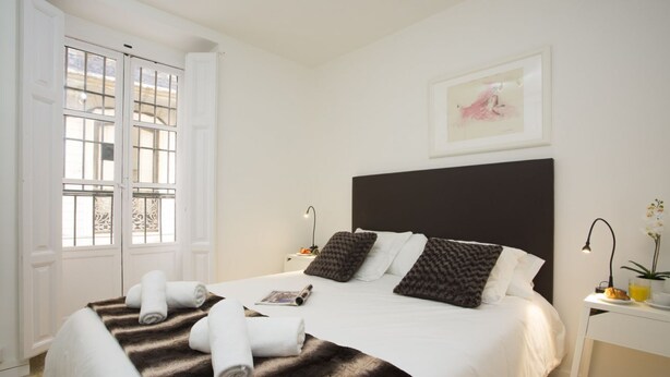A hotel room with a large bed, a nightstand, a bedside table, a framed picture on the wall, and a window with a view. - Singular Stays El Micalet (Valencia)
