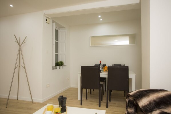 A dining area with a white table, black chairs, and a small window with plants.