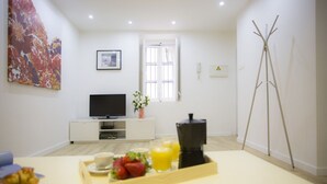 A modern living room with a flat-screen TV, a coffee table with breakfast items, a window with curtains, and a floor lamp. - Singular Stays El Micalet (Valencia)