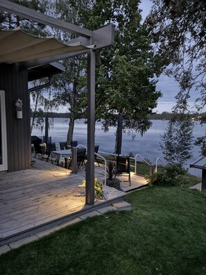 Terraza de madera con mobiliario exterior, con vista a un lago.