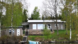 Un chalet au bord du lac, avec un quai, un petit bateau et un mur en pierre.