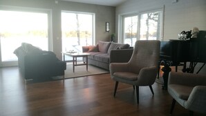 Un salon spacieux doté d’un plancher en bois, d’un fauteuil gris, d’un canapé et d’une table basse. On y trouve également une cheminée et un téléviseur posé sur un meuble.