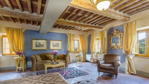 A room with a wooden ceiling, a brown sofa, a patterned rug, a small table, and a chair. - Casa del Fattore   . (Capannori)