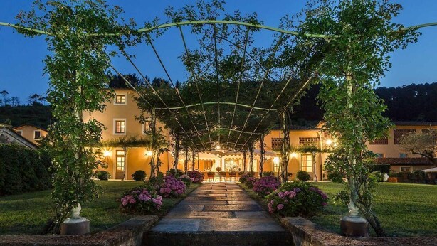 A covered outdoor area with steps leading to a building, surrounded by greenery and flowers. - Casa del Fattore   . (Capannori)