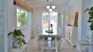 A dining area with a glass table, white chairs, a hanging light fixture, and a view through the window. - Can Butxaquí 160 fantastic villa with private pool and jacuzzi, air conditioning, barbecue and WiFi (Muro)
