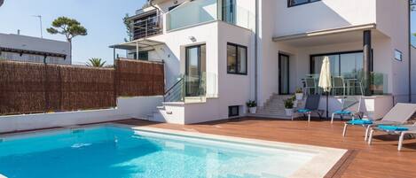 A modern two-story house with a swimming pool, outdoor seating, and a staircase leading to the upper floor.