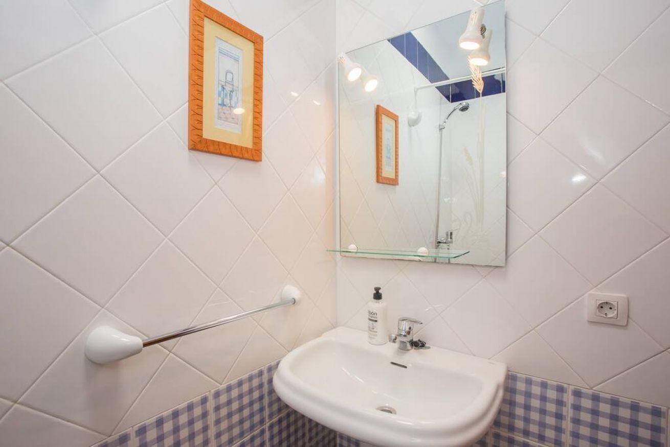 Een badkamer met een witte wastafel, een spiegel en een ingelijst foto aan de muur.