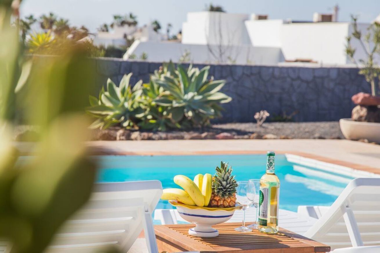 Mesa junto a la piscina con un cuenco de fruta, una botella y un vaso.