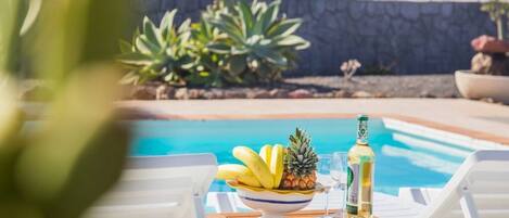 Mesa junto a la piscina con un cuenco de fruta, una botella y un vaso.