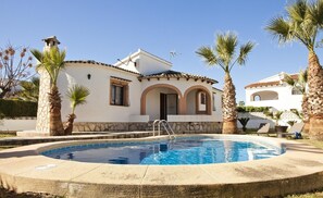 A house with a swimming pool, palm trees, and a clear blue sky.