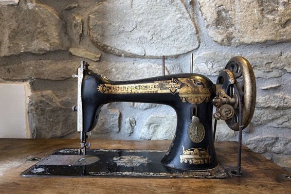 An antique Singer sewing machine with decorative gold accents, placed on a wooden surface against a stone wall.