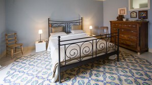 A bedroom with a metal bed frame, a wooden dresser, and patterned floor tiles.