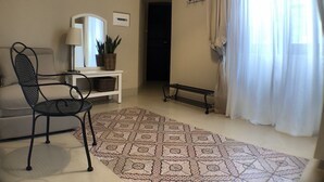 A living room with a patterned rug, a sofa, a chair, a small table, a potted plant, and a window with curtains.