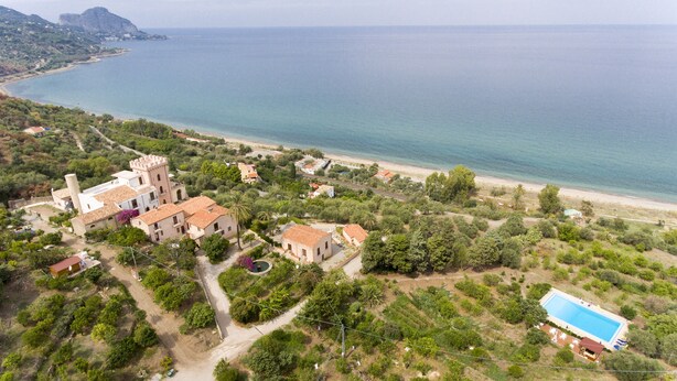 An aerial view of a coastal property with a large building, a swimming pool, and a beach.