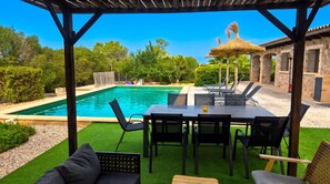 A pool area with a table and chairs, surrounded by greenery and a stone building. - Finca Son Blai Muro 228 by Mallorca Charme (Muro)