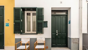 A building with a green door, a window with shutters, and two chairs outside.