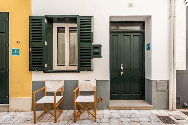 A building with a green door, a window with shutters, and two chairs outside.
