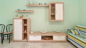 A room with a light green wall, a wooden cabinet with drawers, a sofa with striped cushions, and a small table with chairs.
