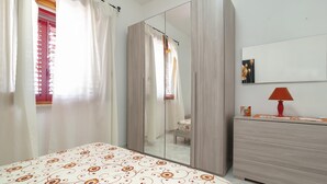 A bedroom with a bed, a wardrobe, a mirror, and a bedside table with a lamp.