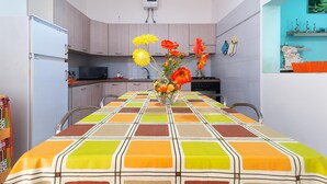 A compact kitchen with modern appliances, a dining table with a colorful tablecloth, and a vase of flowers on the table.