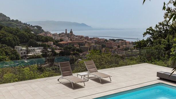 A poolside area with lounge chairs and a view of a coastal town. - Apartment on the Amalfi Coast PARKING SPACE AND POOL (Salerno)