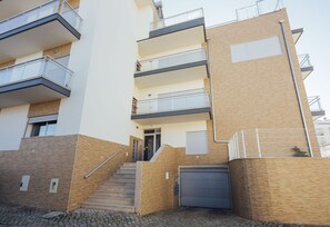 Un immeuble résidentiel à plusieurs étages, doté d’un escalier menant à l’entrée, d’une porte de garage et d’une zone délimitée par une clôture.