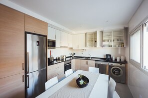 A modern kitchen with stainless steel appliances, white cabinetry, and a dining area with a table set for two.