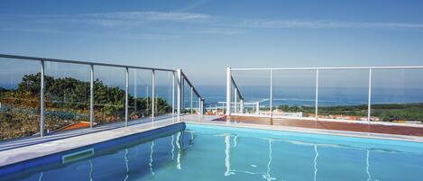 En klarblå pool med en glasvägg som avgränsning, utsikt över havet och en klar himmel.