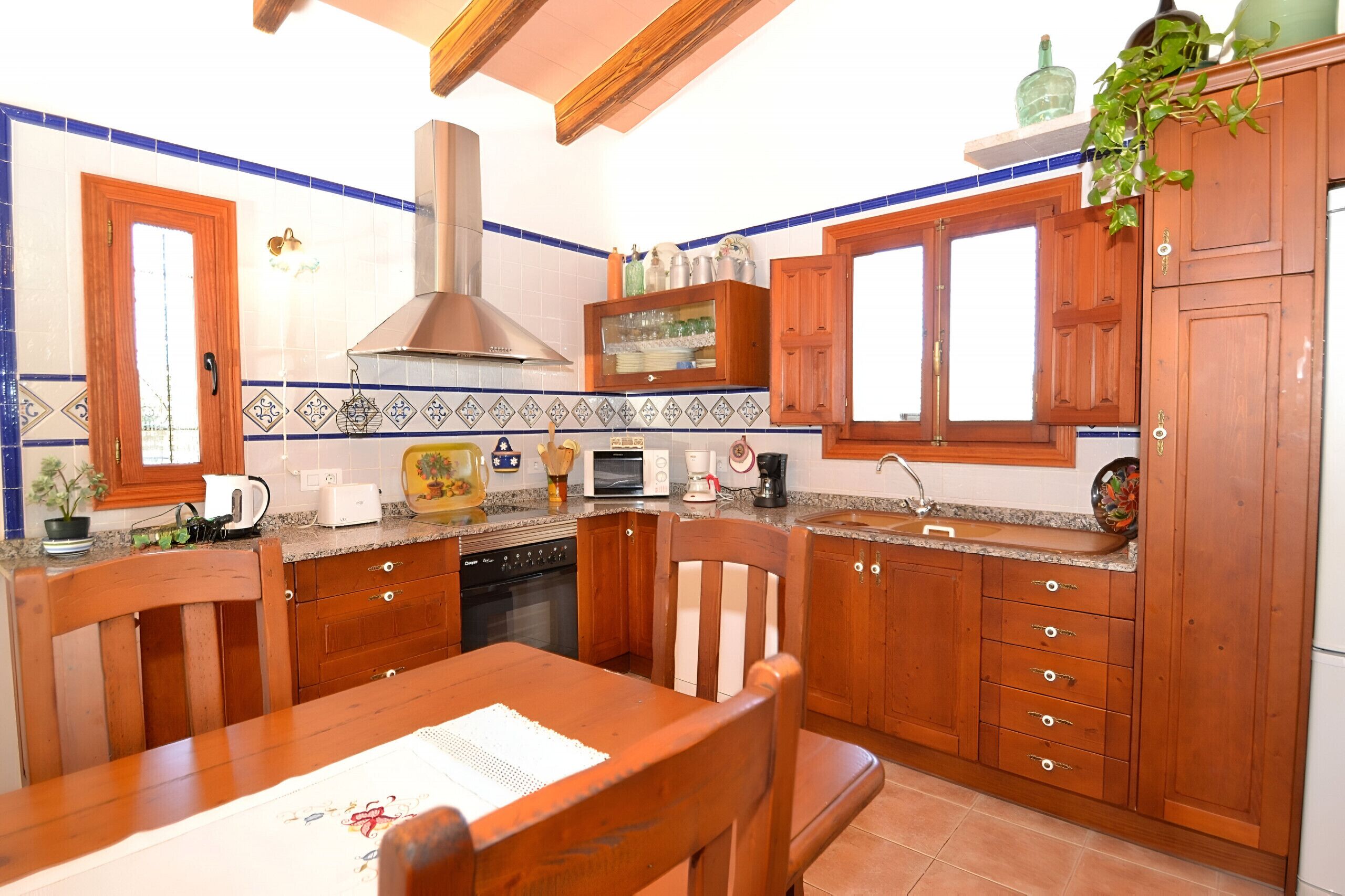 Une cuisine avec des meubles de rangement en bois, une cuisinière, un évier et une table à manger avec des chaises.