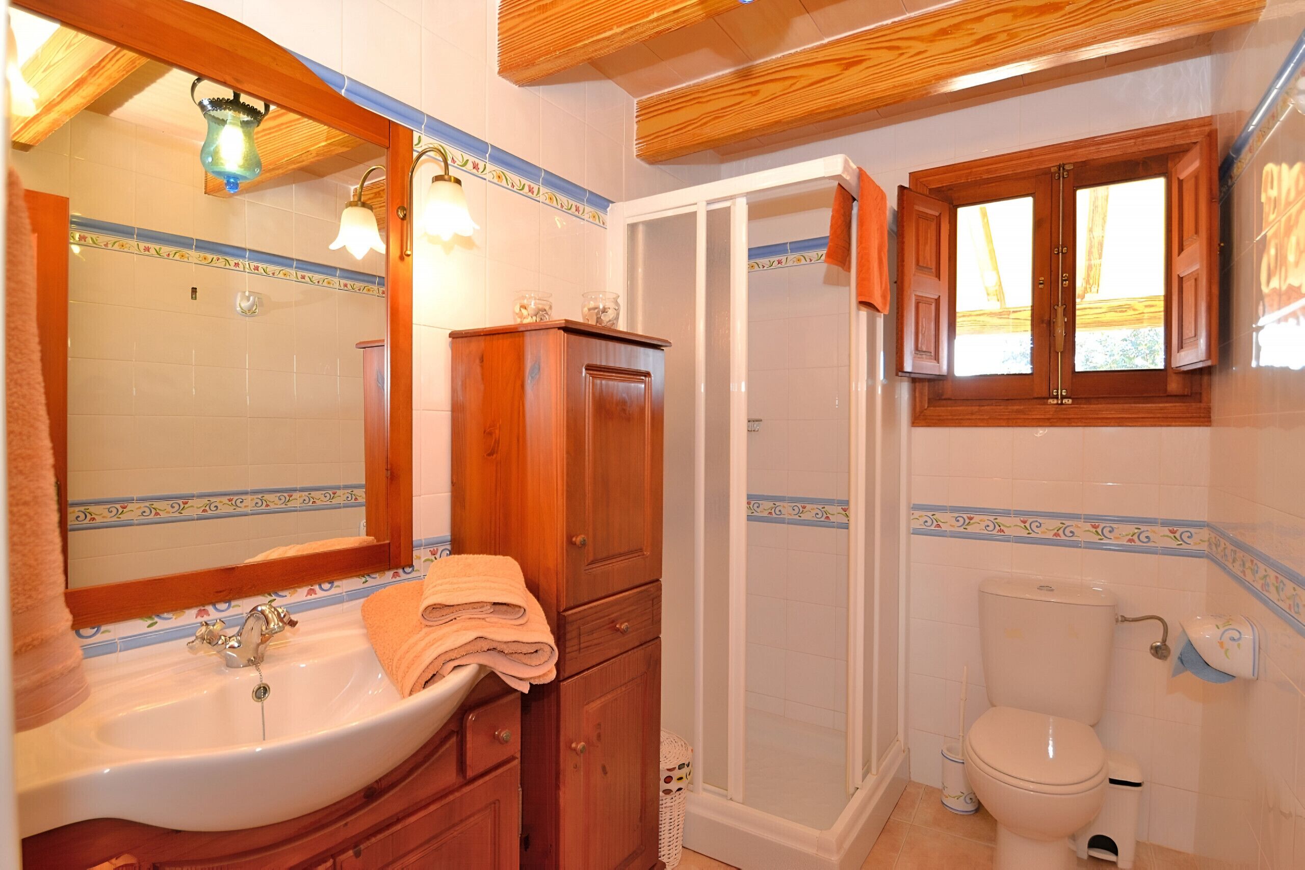 Ein Badezimmer mit Waschbecken, Spiegel, Holzschrank, Dusche, Toilette und einem Fenster mit Vorhängen.
