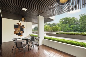 A modern outdoor seating area with a wooden floor, metal chairs, a round table, and a geometric wall art piece. - The Sterling Villas (Pecatu)