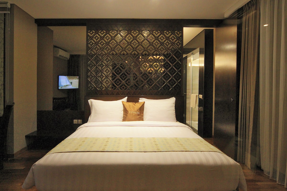 A hotel room with a large bed, a TV on the wall, and a decorative partition.