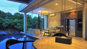 A modern kitchen with a refrigerator, a dining area with a table and chairs, and a glass-enclosed patio with a pool. - The Sterling Villas (Pecatu)
