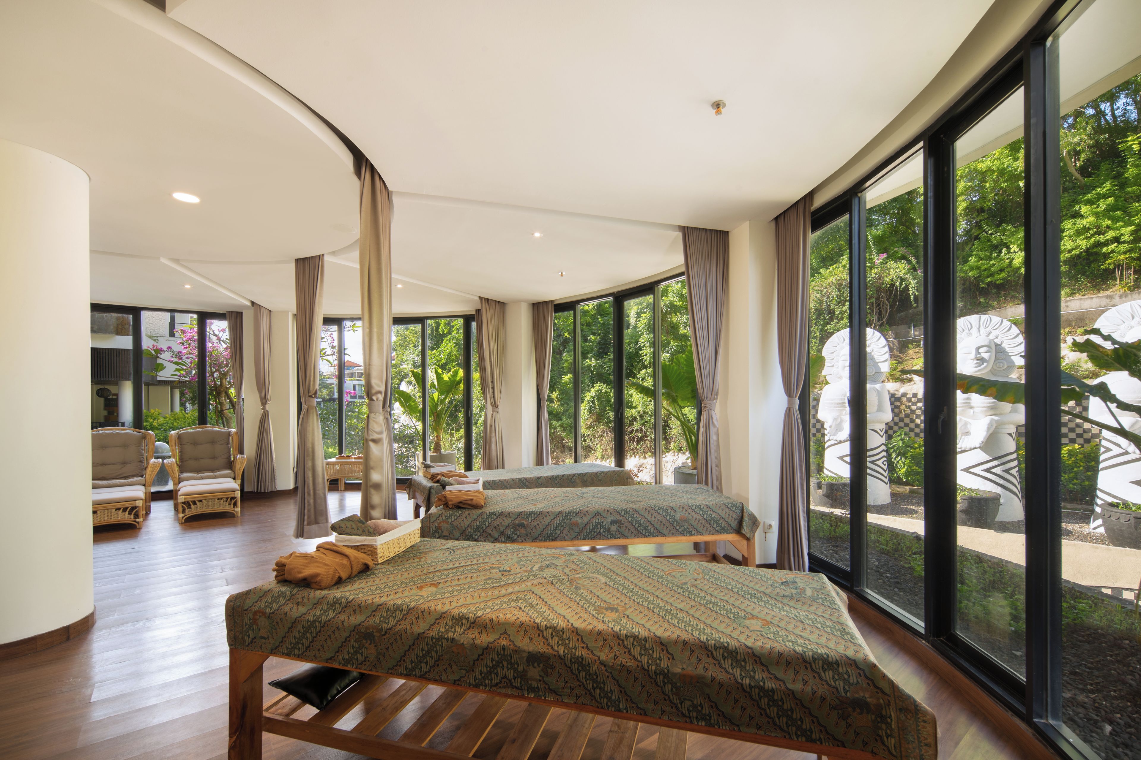 Une chambre spacieuse avec deux lits, un coin salon avec des fauteuils et de grandes fenêtres donnant sur un paysage verdoyant.