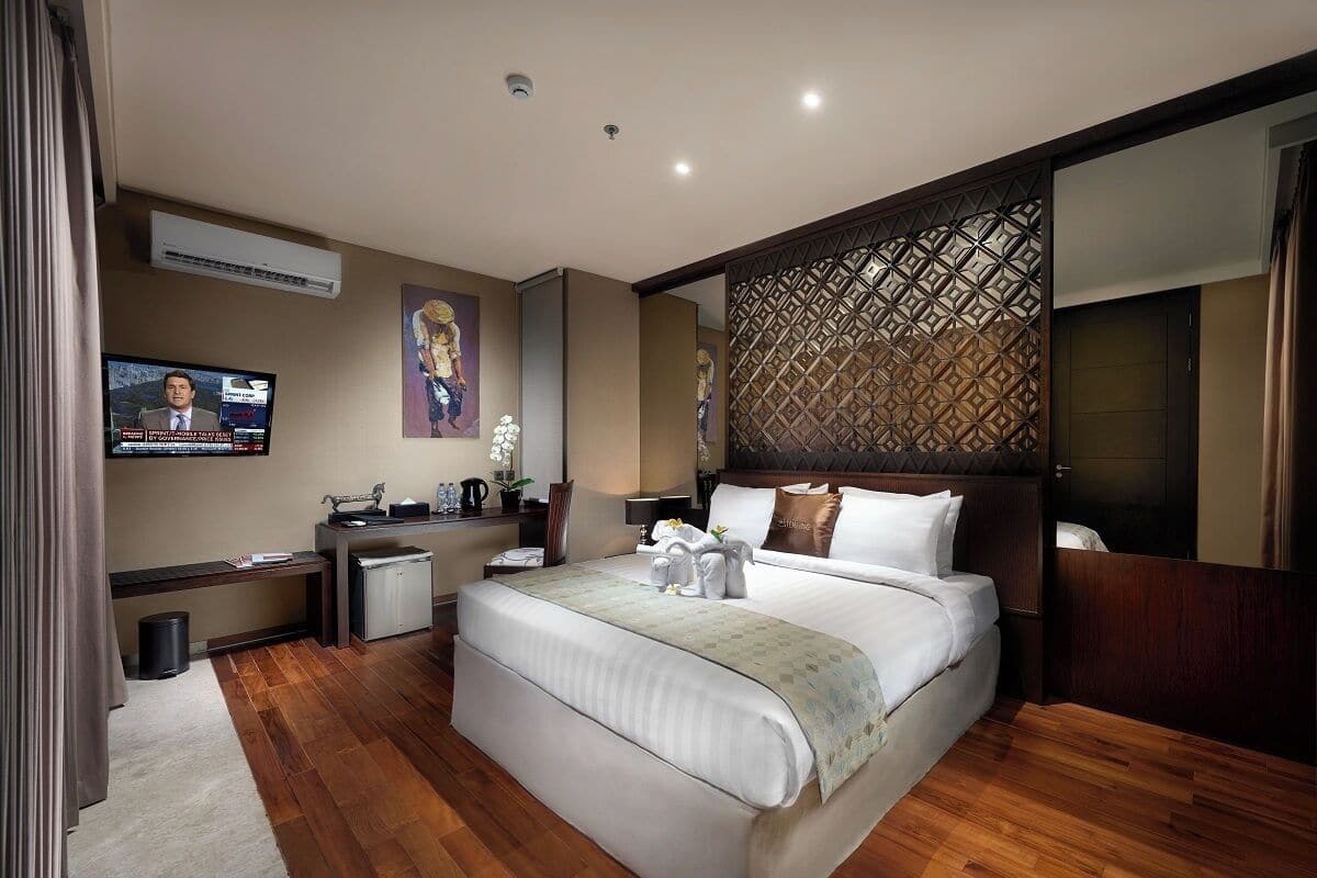 A hotel room with a large bed, a TV, a desk with a computer, and a decorative wall panel.