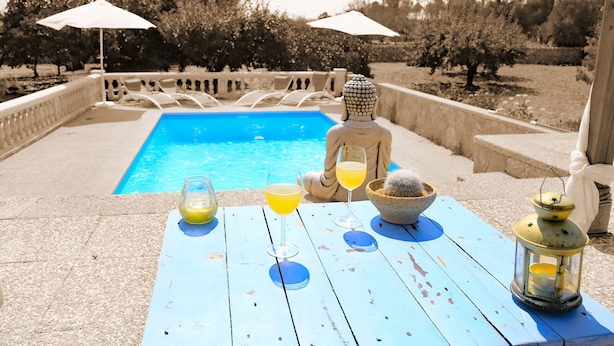 Escena junto a la piscina con una mesa, bebidas y una estatua de Buda.