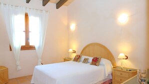 Una cama bien hecha con tablero de madera, dos mesitas de noche con lámparas y una ventana con cortinas.