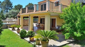 Una casa de dos pisos con balcón, zona de estar exterior y plantas en macetas.