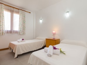Une chambre d’hôtel avec deux lits simples, une table de chevet avec une lampe et une fenêtre avec des rideaux.