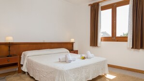 A hotel room with a large bed, a wooden headboard, a nightstand with a lamp, and a window with curtains.