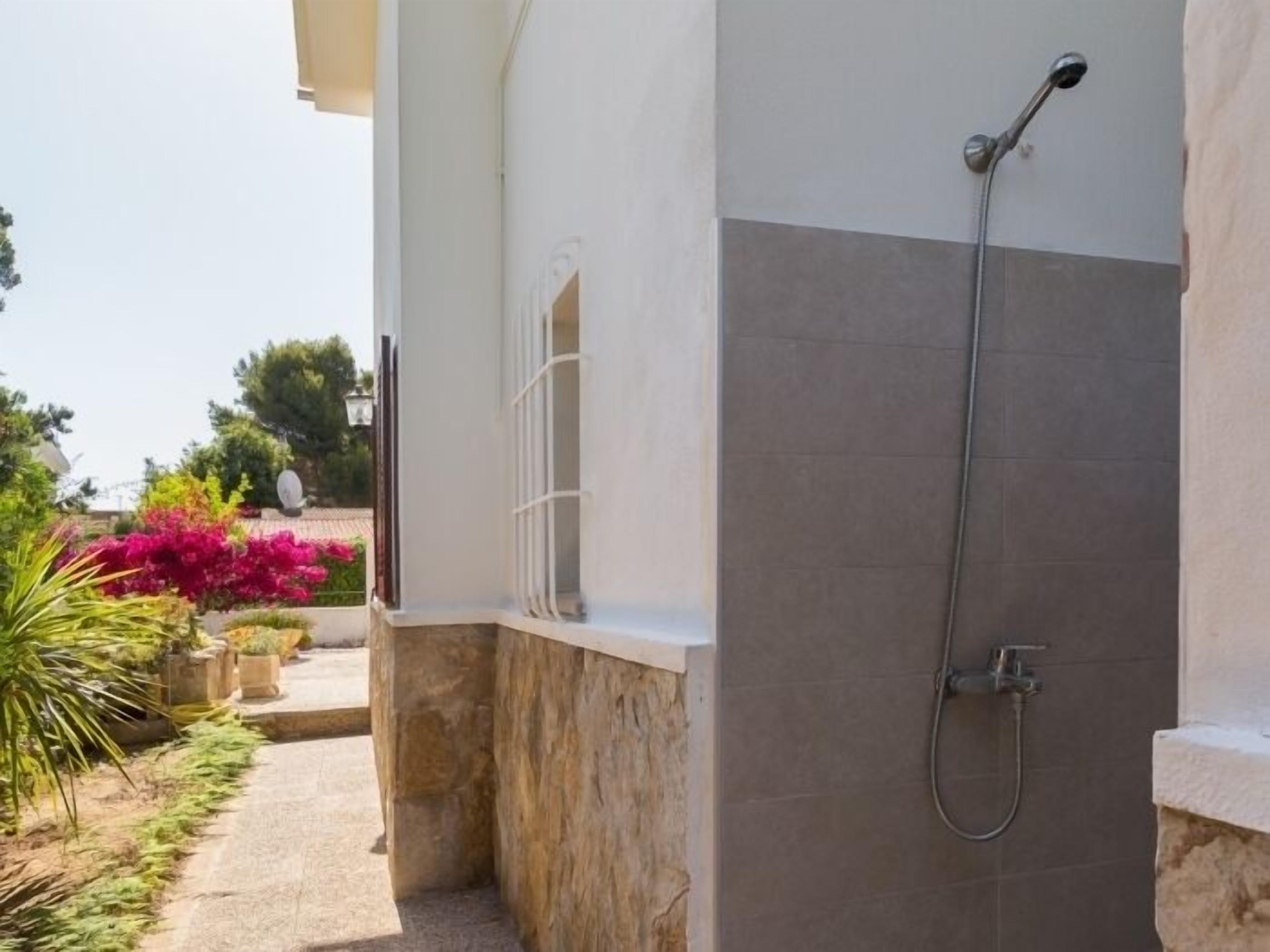 A bathroom with a shower, stone walls, and a view of a garden with pink flowers.