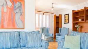 A living room with striped blue sofas, a wooden bookshelf, and a painting on the wall.