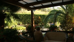 A covered patio with wicker furniture, a large vase, and lush greenery.
