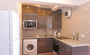 Een kleine keuken met een magnetron, oven, spoelbak en wasmachine.