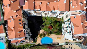 Vista aérea de un hotel con varios tejados de tejas rojas, una piscina central y un jardín ajardinado.