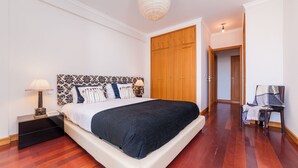Une chambre à coucher avec un lit, des lampes de chevet, une armoire en bois et une chaise avec une couverture.