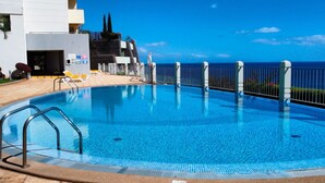 Une piscine avec vue sur l’océan, entourée d’un bâtiment blanc doté d’un balcon et de chaises longues.