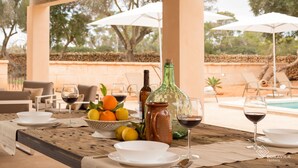 An outdoor dining area with a table set for two, featuring a bottle, glasses, and a bowl of fruit. - Finca Son Grauet - Spectacular villa with pool in Llucmajor (LLucmajor)